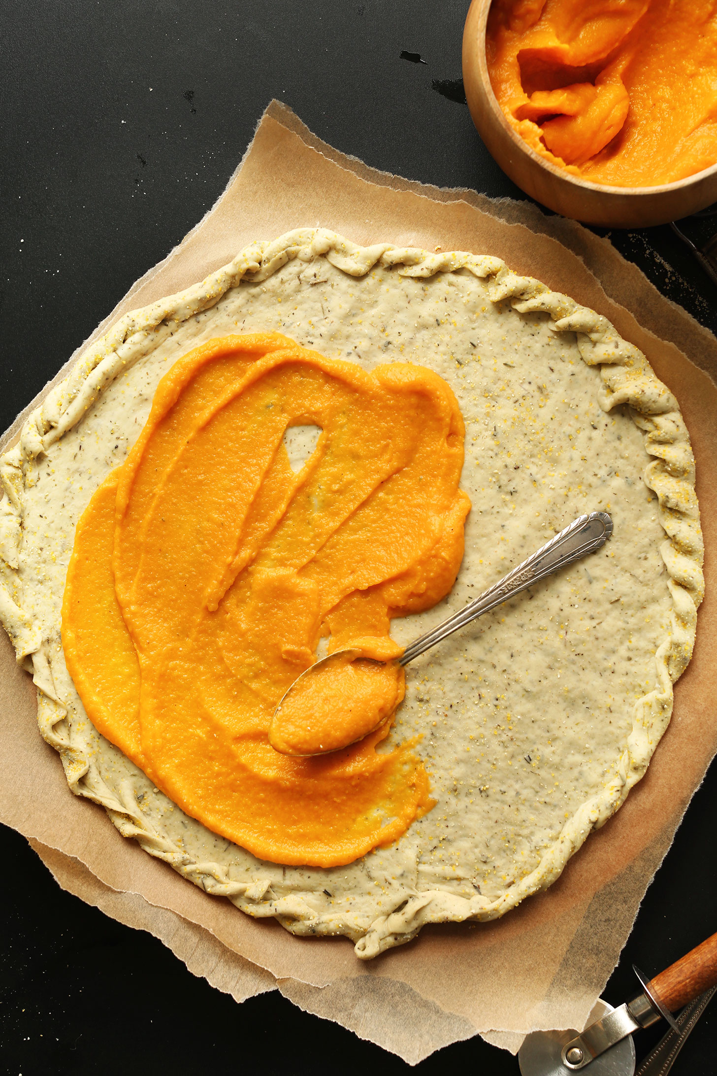 Spreading butternut squash pizza sauce onto crust for homemade vegan pizza night