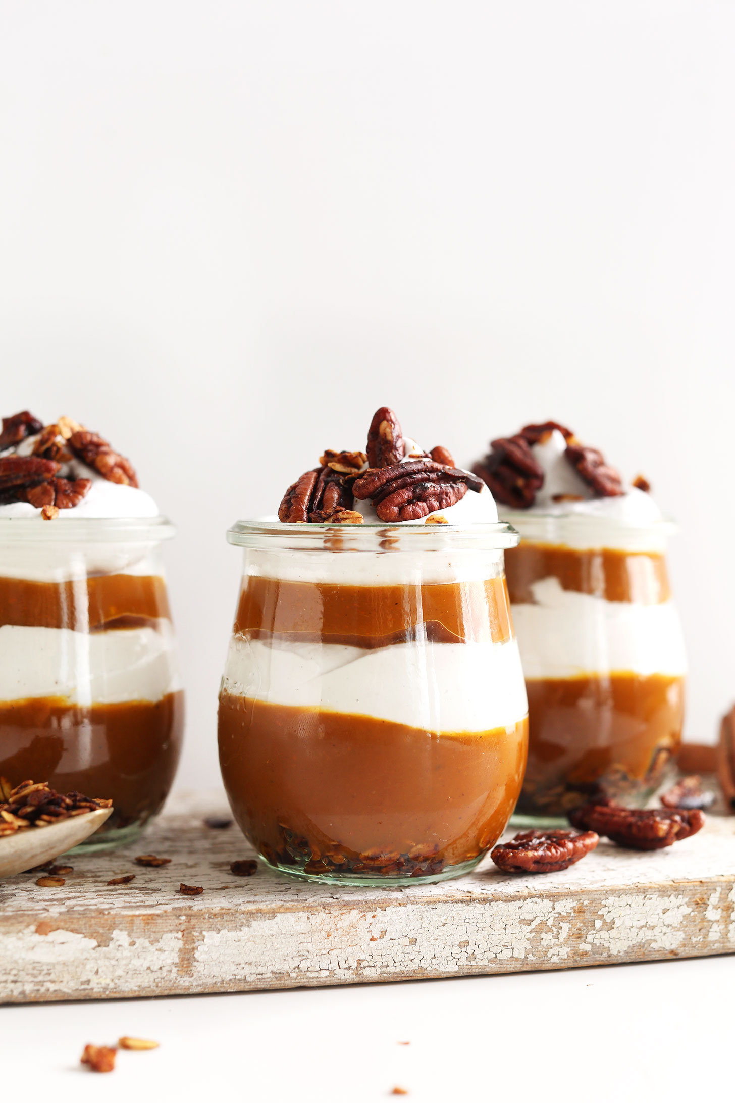 Cutting board with jars of Pumpkin Pie Parfaits made with granola, pumpkin butter, and coconut whip