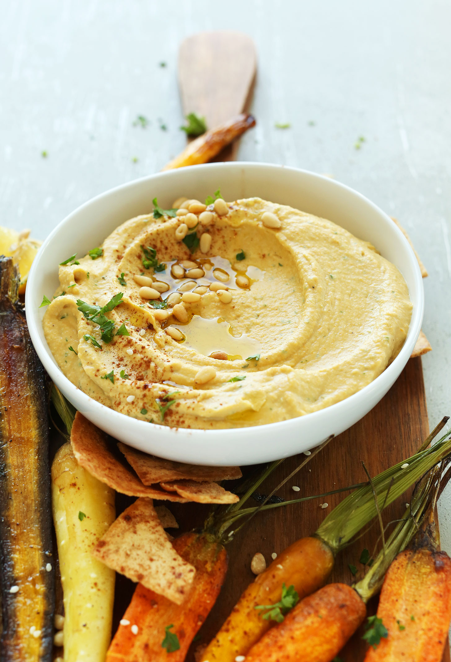 Close up shot of a delicious bowl of Butternut Squash Hummus topped with olive oil, pine nuts, and fresh parsley