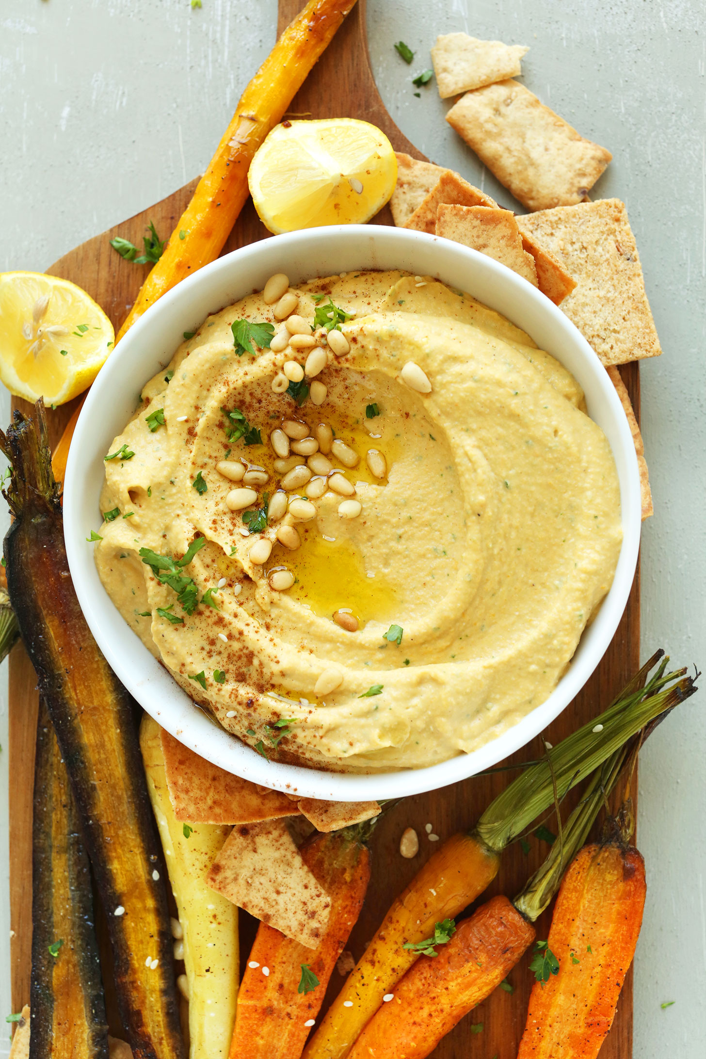 Wood cutting board with a bowl of our Butternut Squash Hummus recipe and goodies for dipping