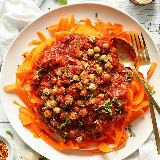 Gold spoon and fork resting on a plate of Chickpea Bolognese over Carrot Noodles
