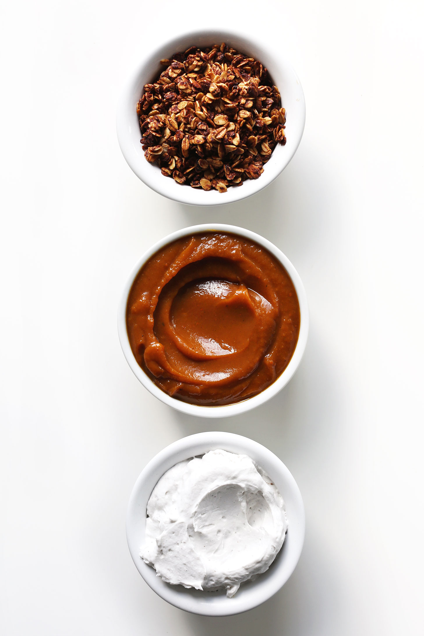 Bowls of pumpkin granola, pumpkin butter, and coconut whipped cream for making Pumpkin Pie Parfaits