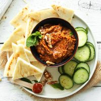 Plate of sliced cucumbers, pita, and a bowl of Smoky Harissa Eggplant Dip