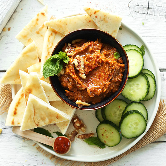 Plate of sliced cucumbers, pita, and a bowl of Smoky Harissa Eggplant Dip
