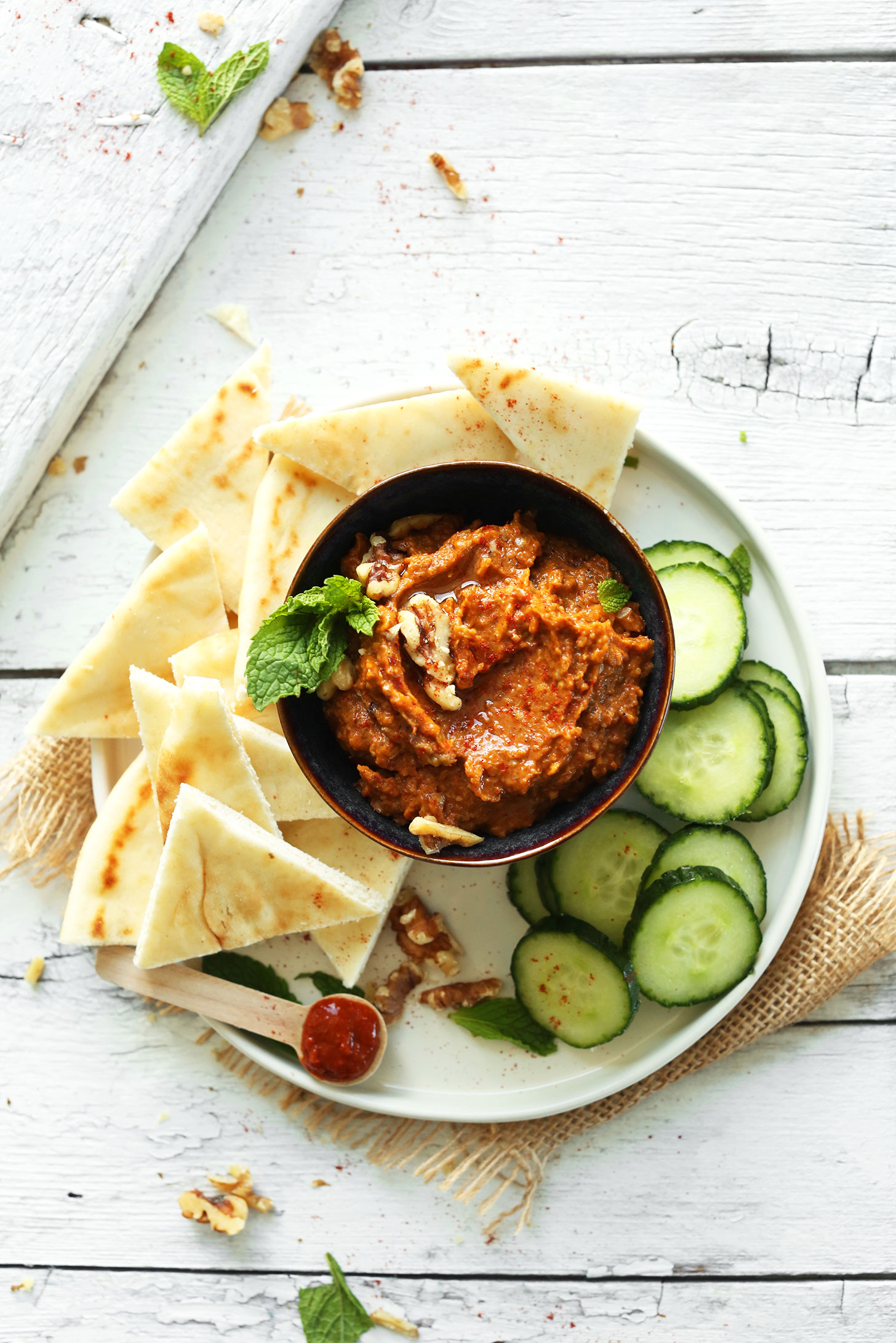 Bowl of our Smoky Harissa Eggplant Dip recipe surrounded by sliced cucumbers and pita bread for dipping
