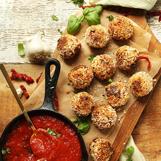Skillet of marinara sauce beside a batch of Sun-Dried Tomato & Basil Arancini