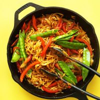 Tongs in a skillet of Vegan Singapore Noodles made with snow peas