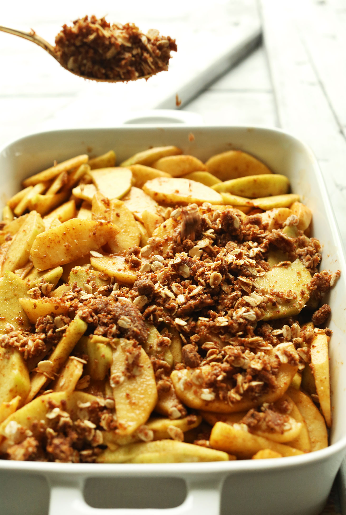 Sprinkling Pecan-Oat Topping onto the Best Vegan Apple Crisp for a fall dessert