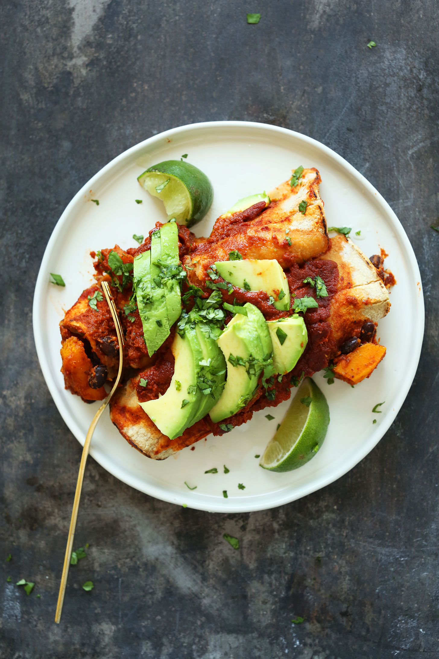 Plate of butternut squash enchiladas topped with avocado and cilantro