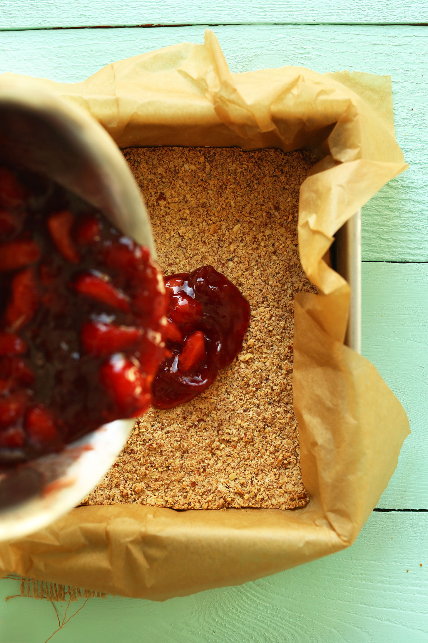 Pouring strawberry mixture over the crust for Gluten-Free Vegan PB&J Bars