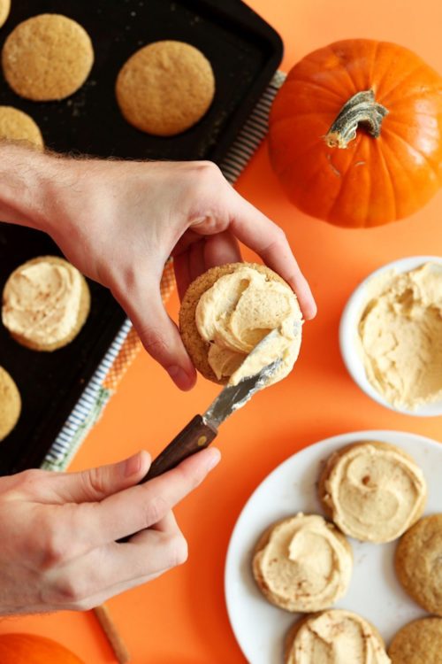 Spreading frosting onto a vegan pumpkin sugar cookie