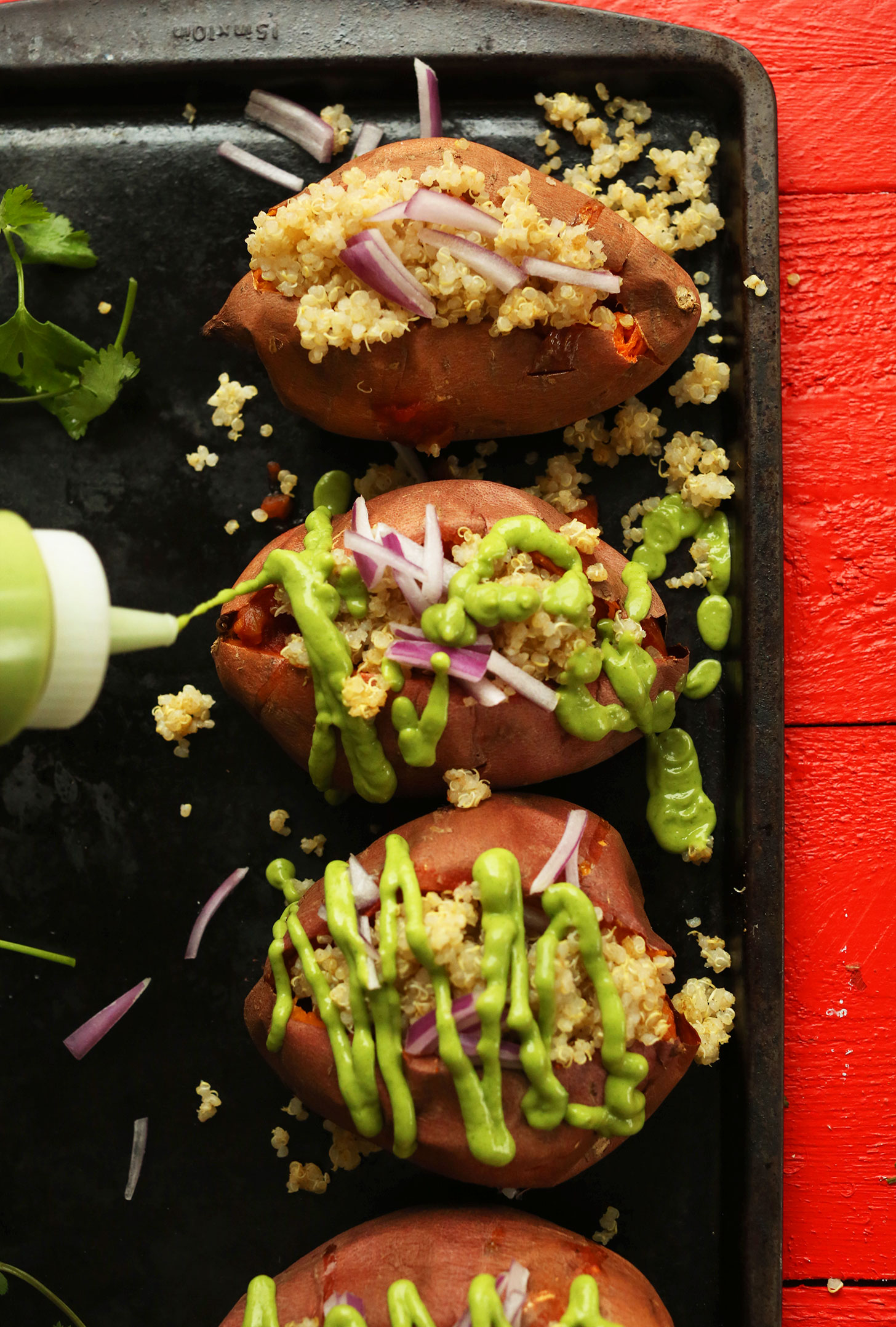 Drizzling avocado cilantro sauce over a tray of Quinoa Stuffed Sweet Potatoes