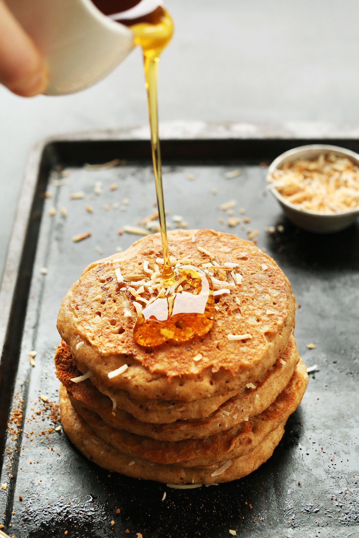 Drizzling maple syrup onto a stack of Vegan Toasted Coconut Pancakes
