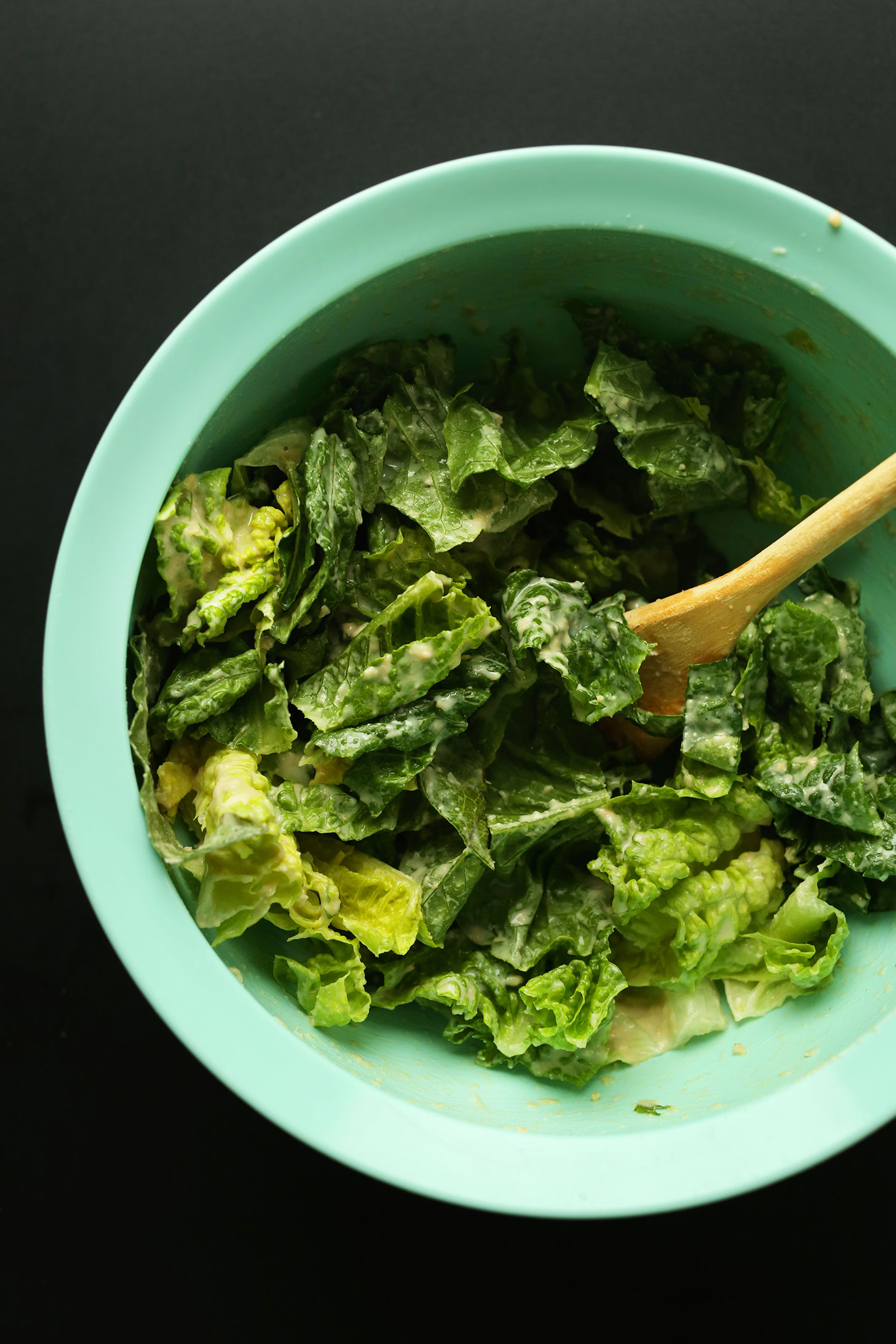 Stirring romaine lettuce with hummus dressing for adding to vegan Buffalo Chickpea Wraps