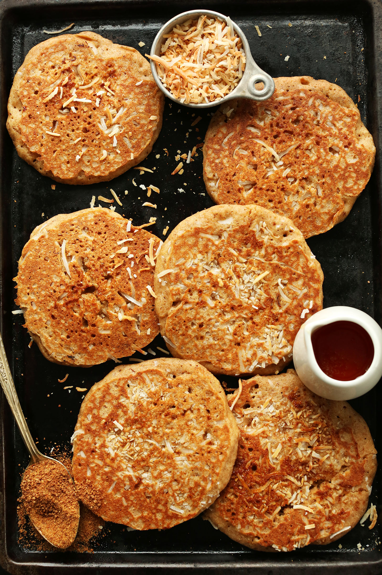 Baking sheet with freshly made vegan Toasted Coconut Pancakes and maple syrup for serving
