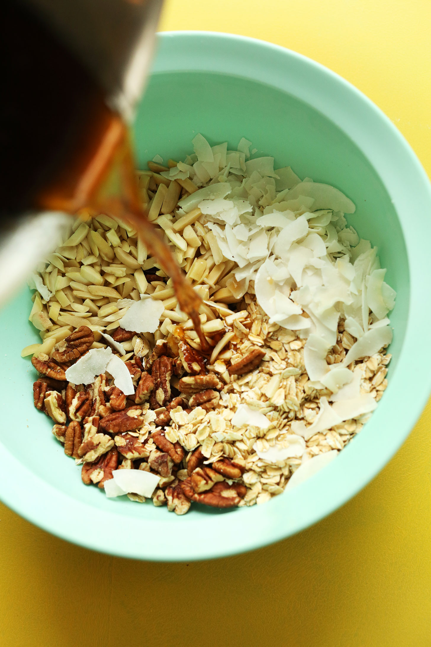 Pouring melted coconut oil maple syrup mixture into dry ingredients for homemade vegan coconut granola