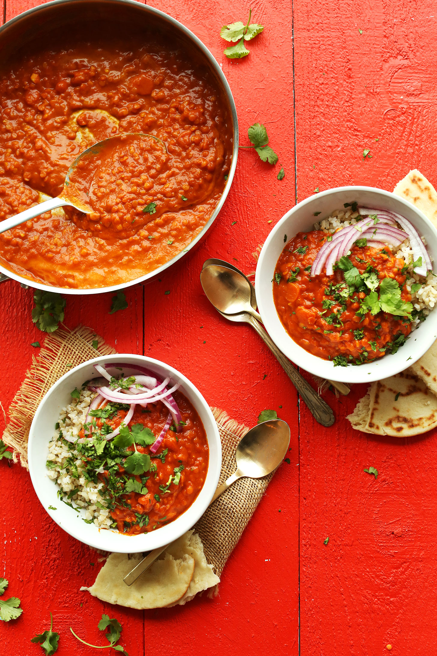 Pan of Spicy Red Lentil Curry and two serving bowls filled with rice, curry, and garnish of cilantro and red onion