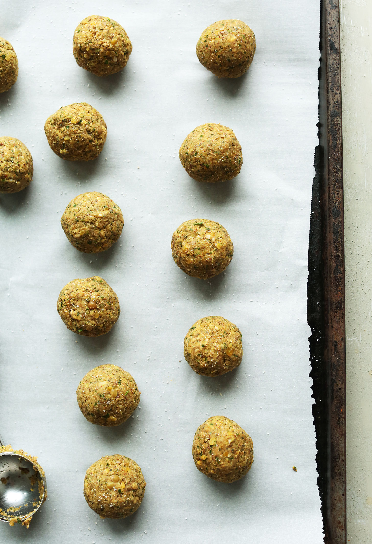 Parchment-lined baking sheet with freshly rolled vegan lentil meatballs
