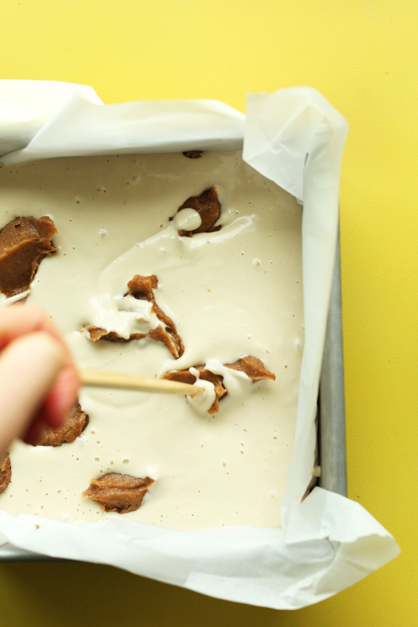 Using a toothpick to swirl date caramel into vegan snickers cheesecake filling