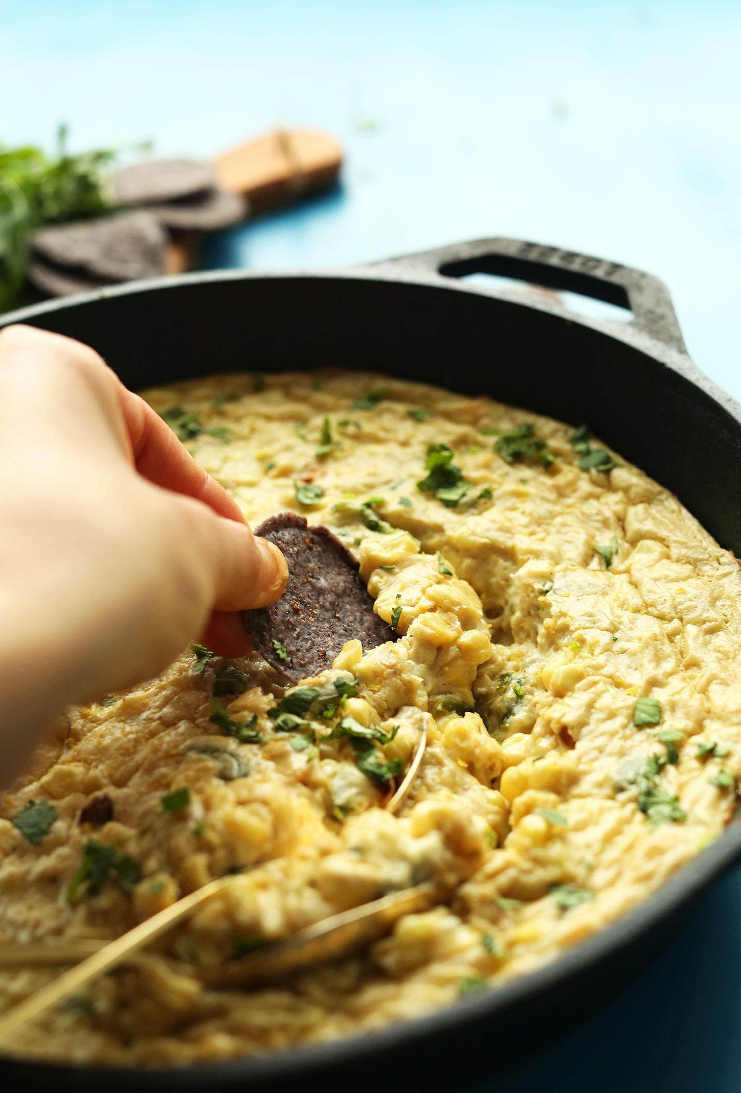 Dipping a blue corn chip into Cheesy Corn Dip with Jalapenos