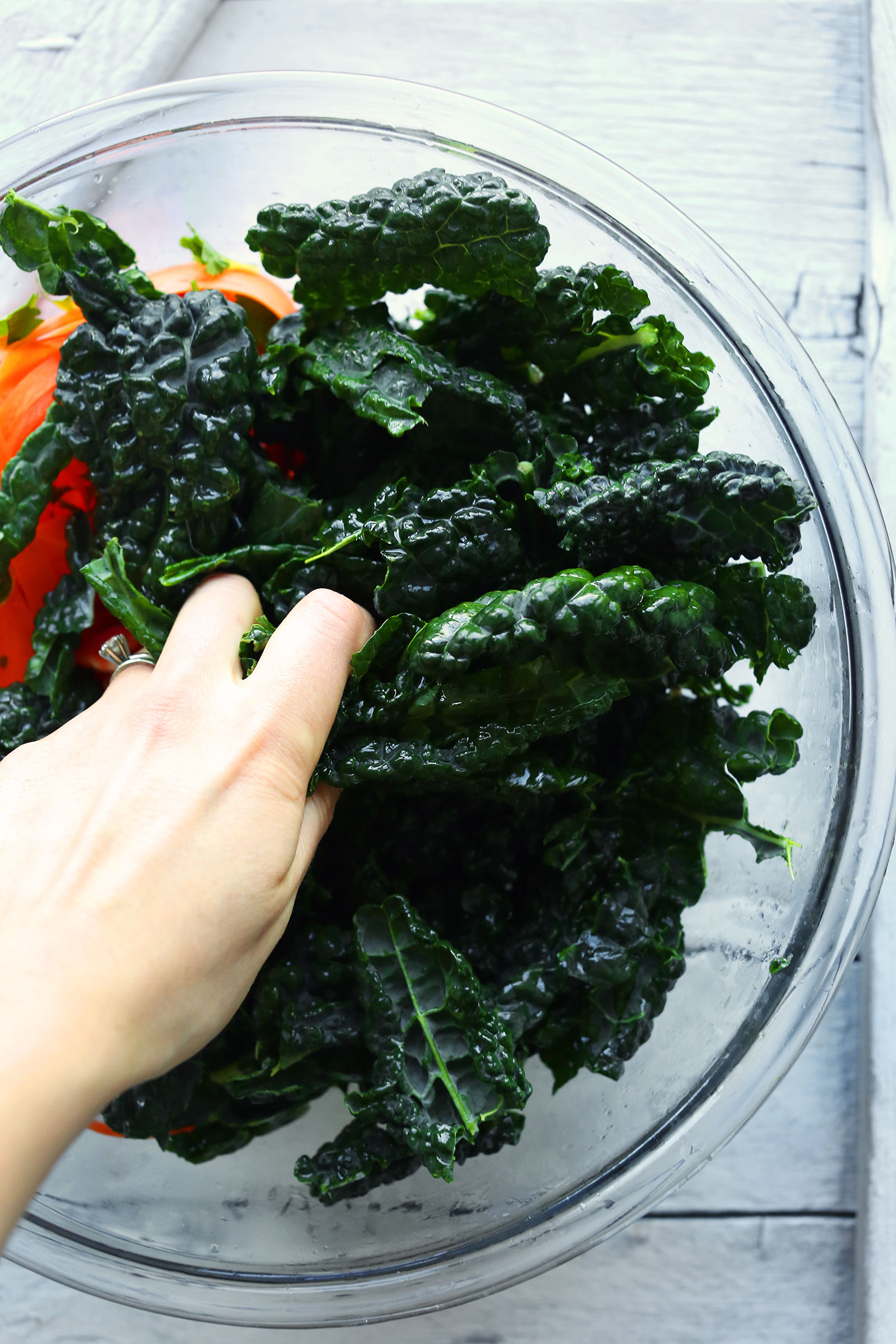 Adding kale leaves to a bowl for Gingery Thai Kale Salad made with tons of veggies