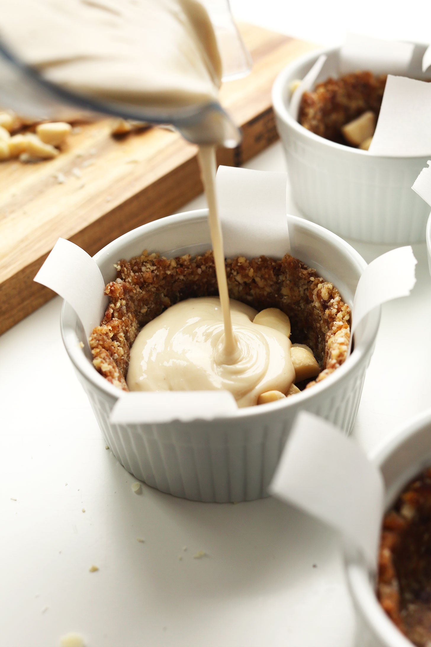 Pouring vegan cheesecake filling into a crust-filled ramekin
