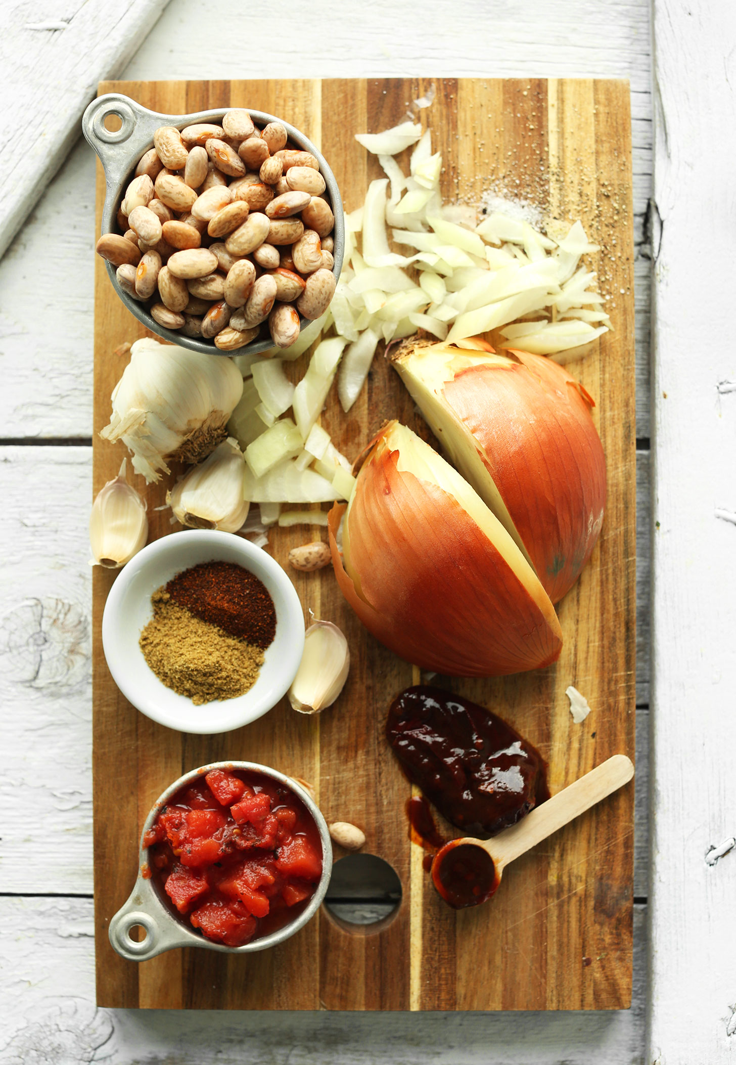 Cutting board with onion, garlic, pinto beans, spices, chipotle chili, and tomatoes for making homemade Mexican Pinto Beans from Scratch