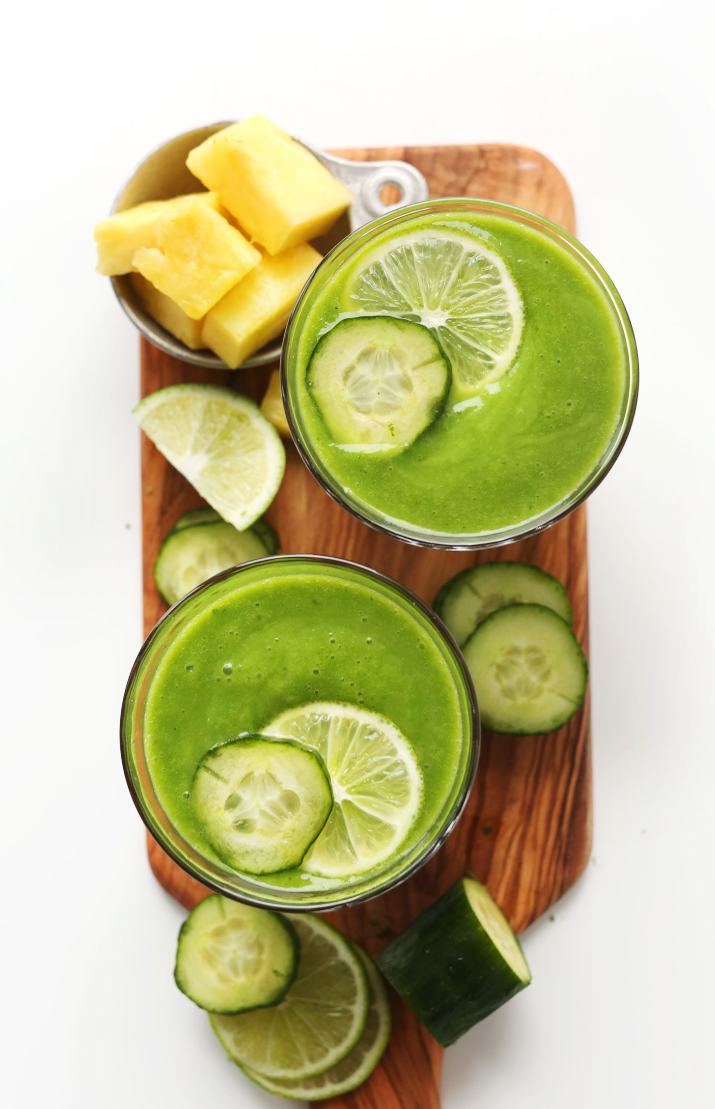 Jars filled with our Healthy Creamy Cucumber Smoothie recipe surrounded by pineapple chunks and cucumber