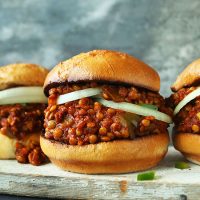Wood board with three buns filled with sliced onions and our Vegan Sloppy Joe recipe