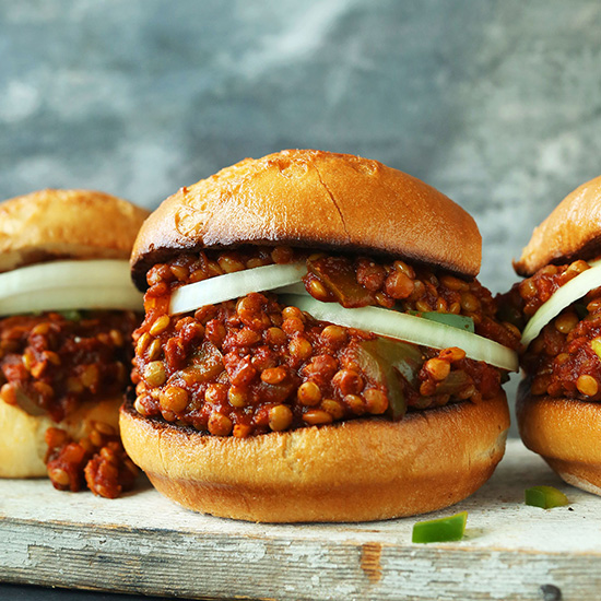 Wood board with three buns filled with sliced onions and our Vegan Sloppy Joe recipe