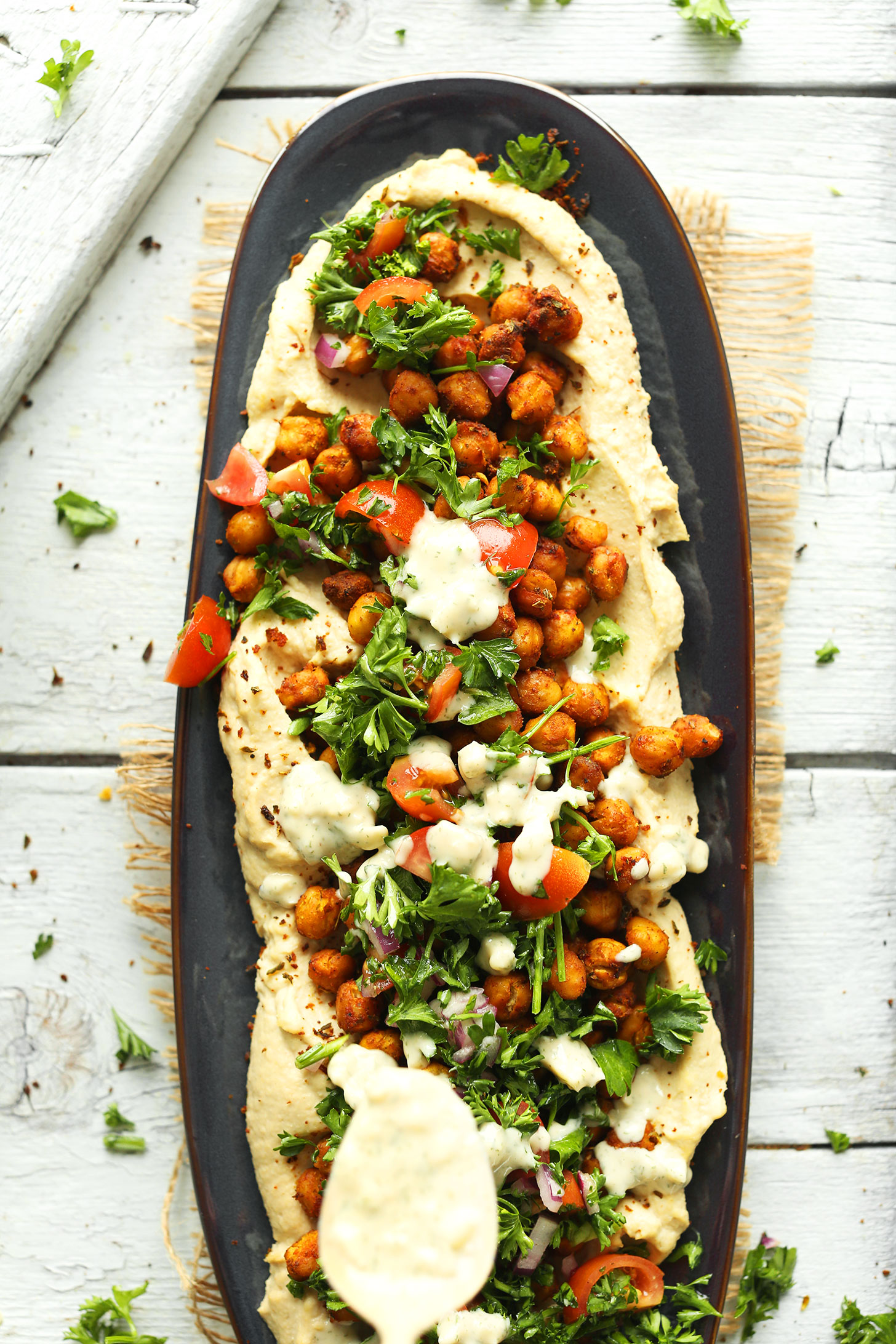 Drizzling Garlic Herb Sauce to make Chickpea Shawarma Dip for a summertime vegan appetizer
