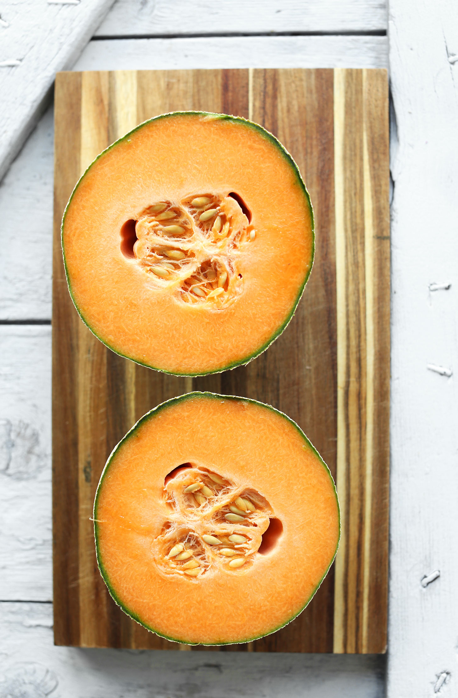 Halved fresh cantaloupe on a cutting board for making a refreshing vegan salad