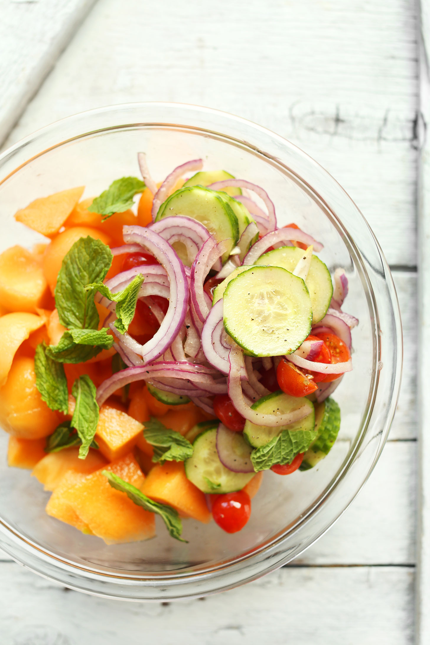 Bowl with mint, onions, cucumbers, tomatoes, and cantaloupe for making a savory-sweet vegan summer salad