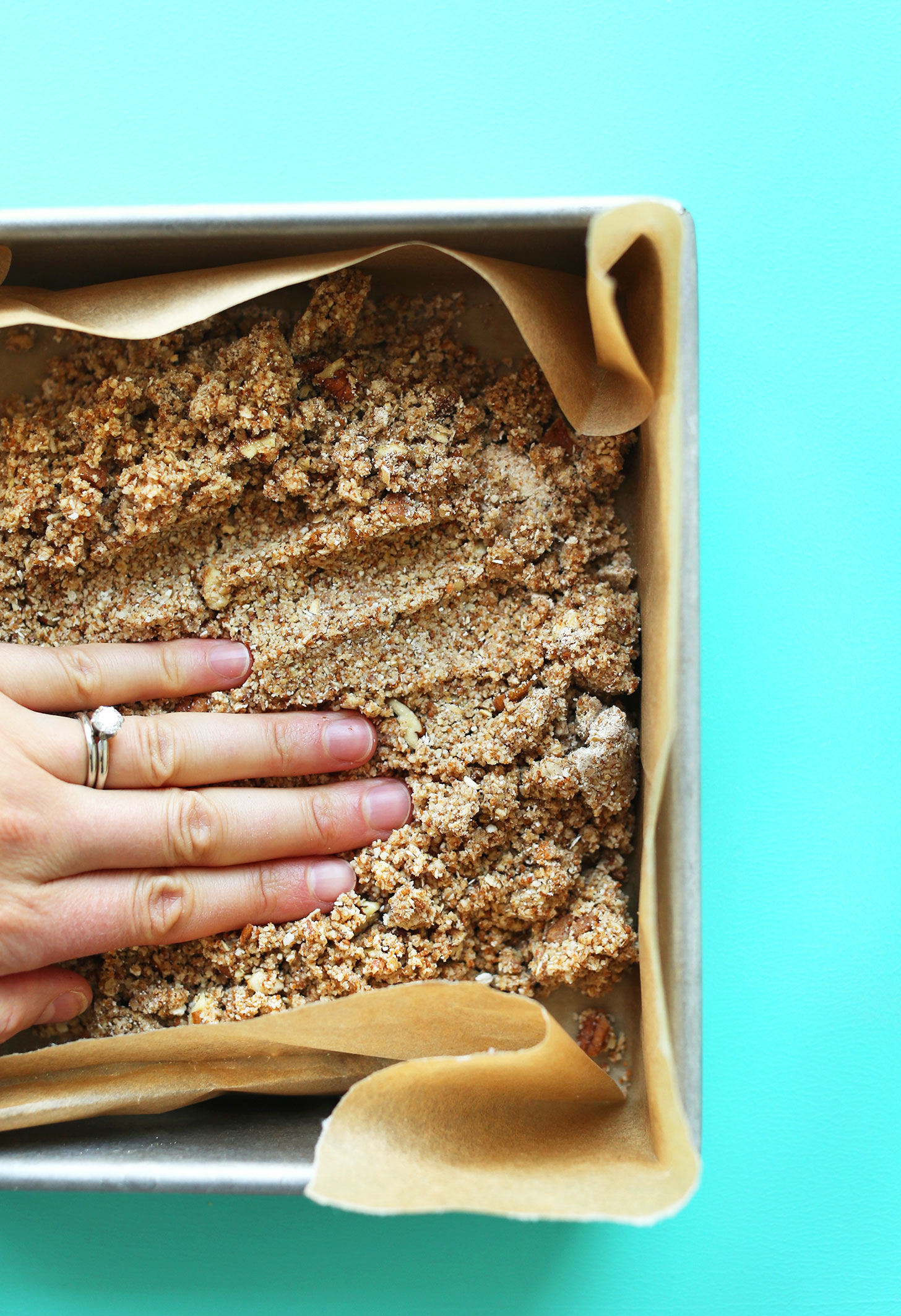 Pressing down almond-oat crust into a parchment-lined baking pan for Gluten-Free Vegan S'Mores Bars