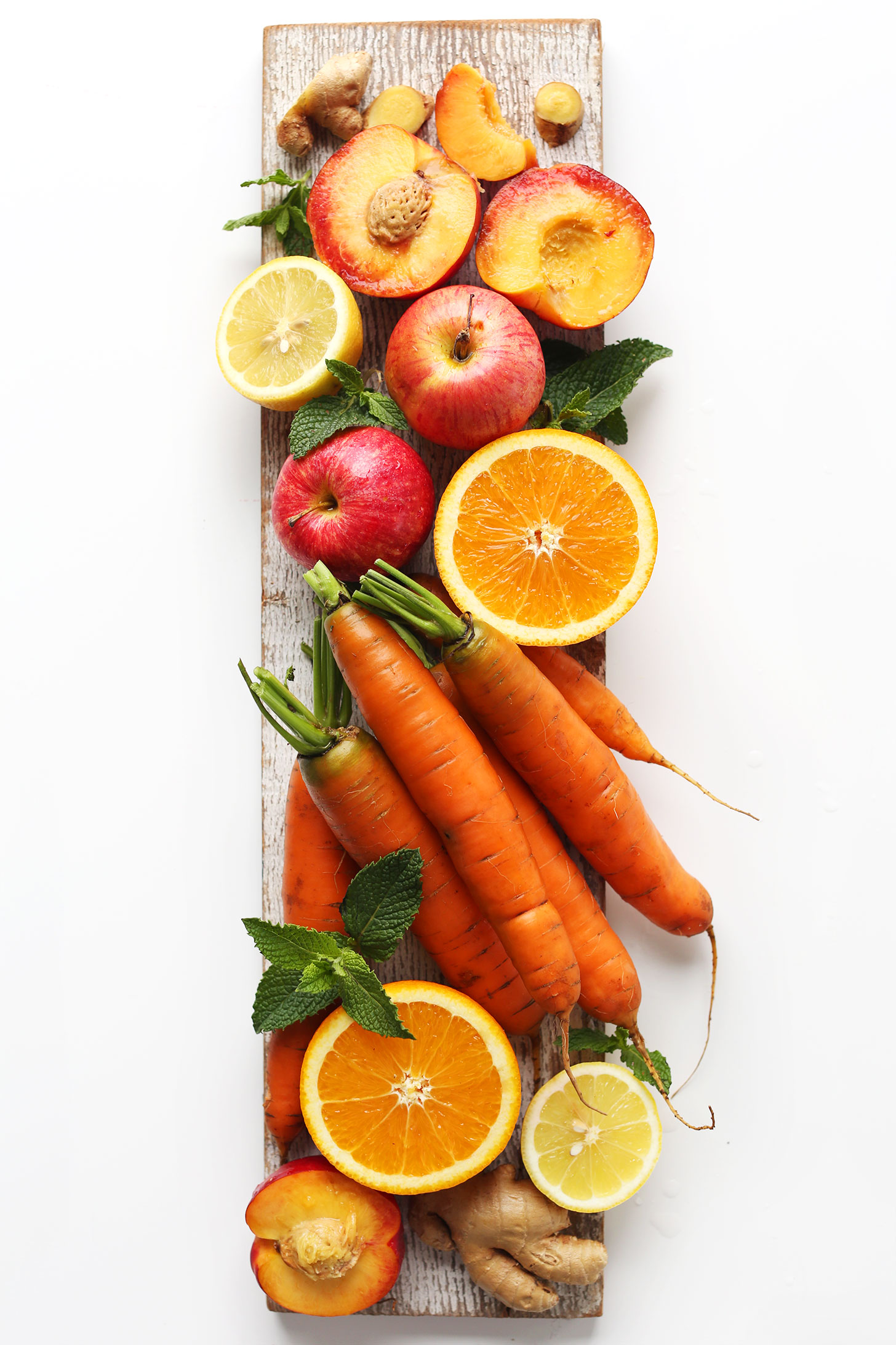 Wood plank with nectarines, ginger, lemon, apples, orange, and carrots for making our Super-Powered Orange Juice