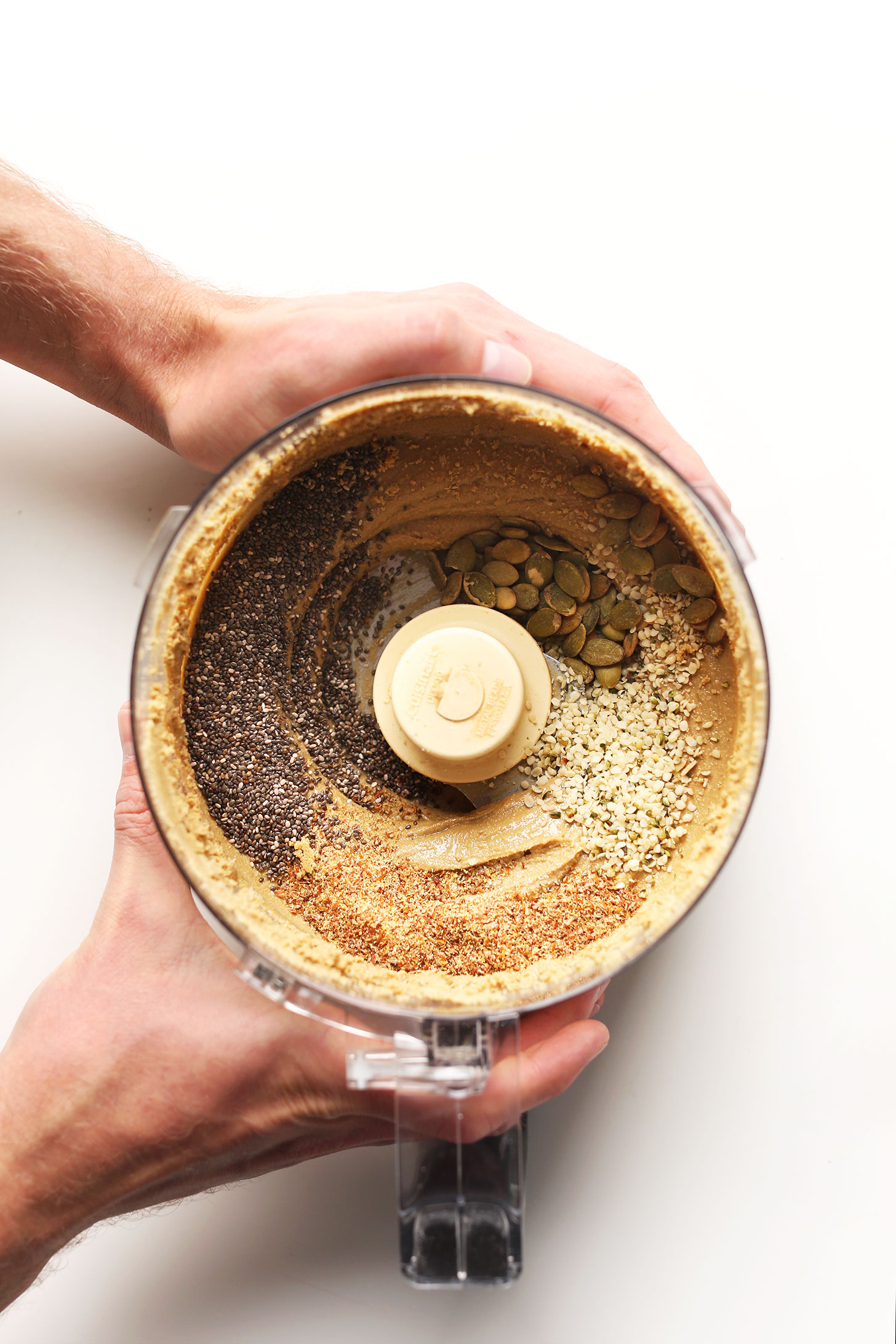Food processor with freshly blended Sunflower Seed Butter topped with chia, flax, pumpkin, and hemp seeds