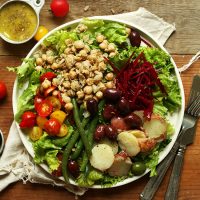 Big plate of Vegan Nicoise Salad with a measuring cup of dressing on the side