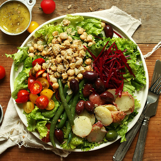 Big plate of Vegan Nicoise Salad with a measuring cup of dressing on the side