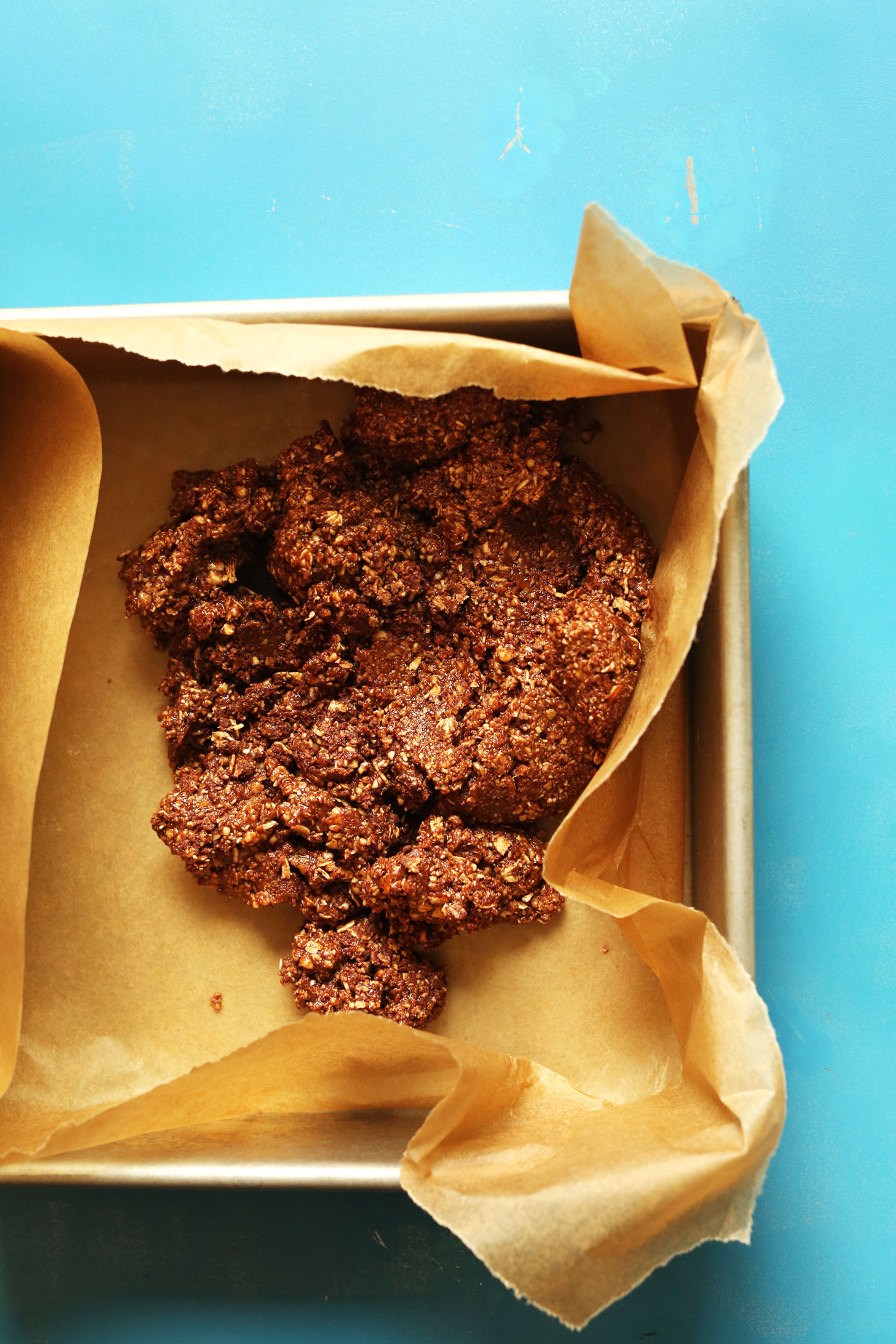 Parchment-lined baking pan with crust batter for gluten-free vegan Almond Butter Cup Bars