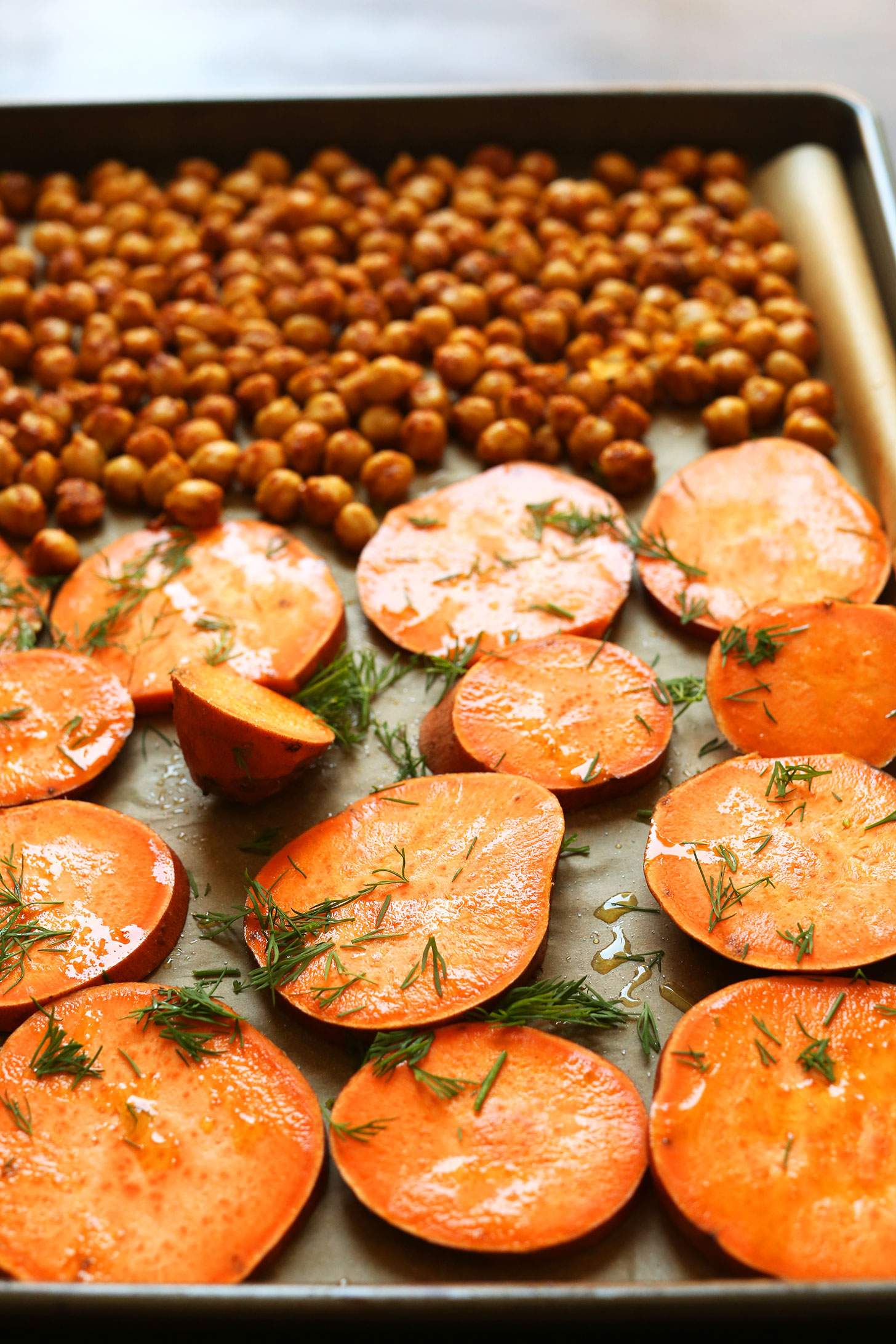 Parchment-lined baking sheet with chickpeas and sliced sweet potatoes topped with fresh dill
