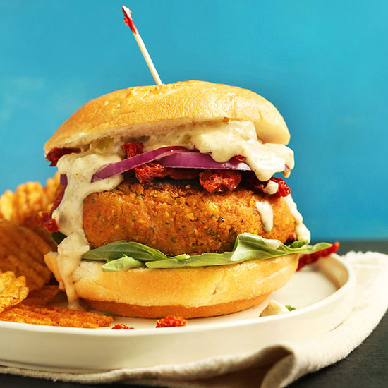 Plate of potato chips and a Vegan Sun-Dried Tomato Chickpea Burger on a bun with toppings