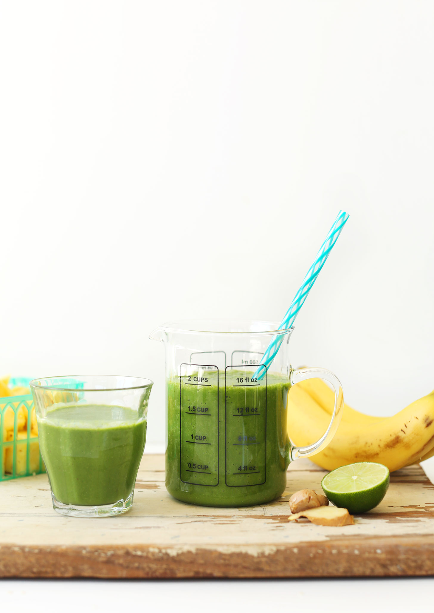Wood board with measuring and serving glasses full of our vegan Ginger Colada Green Smoothie recipe