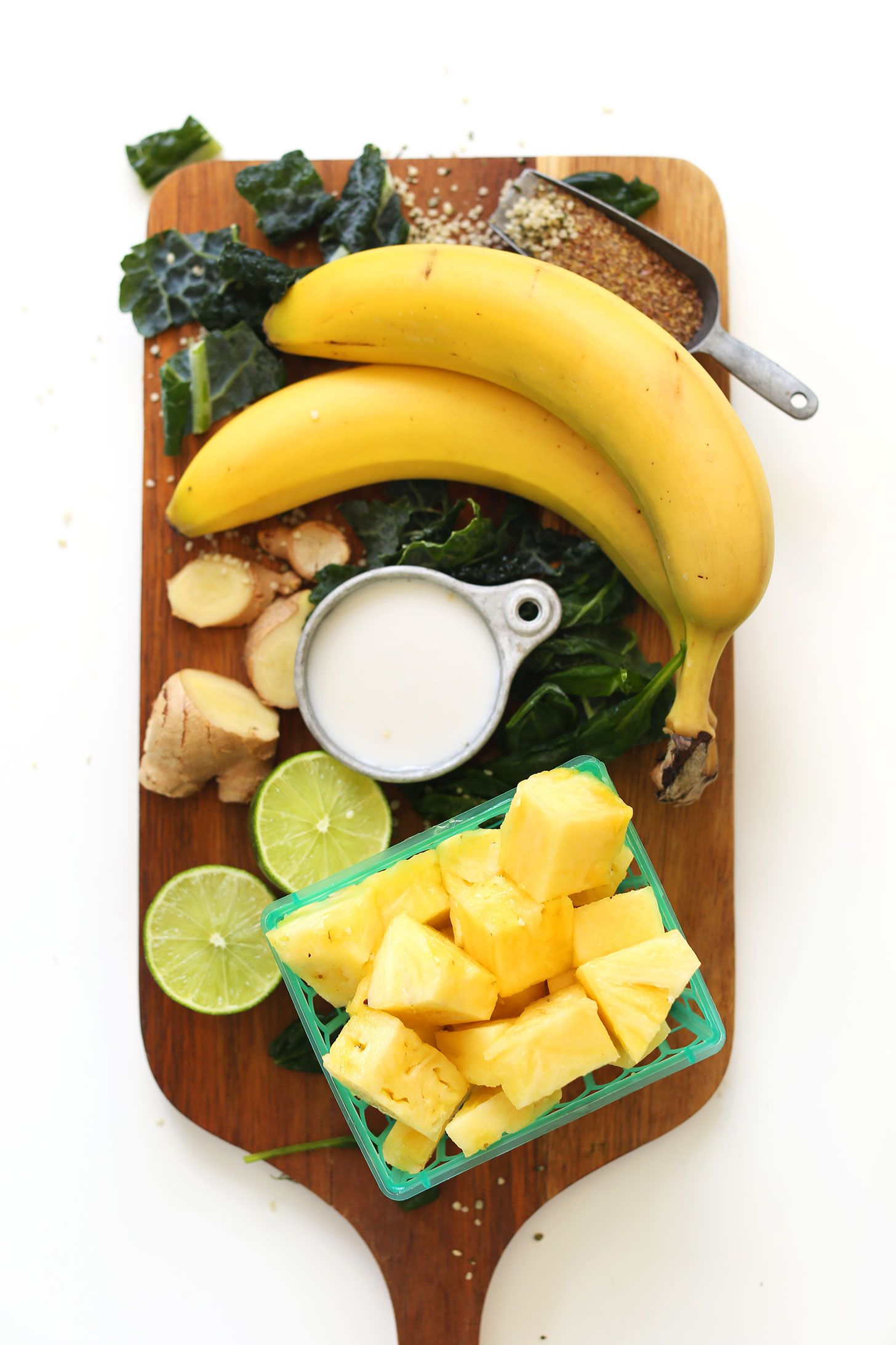Wood board with pineapple, banana, nut milk, lime, ginger, kale, hemp seeds, and flaxseed meal