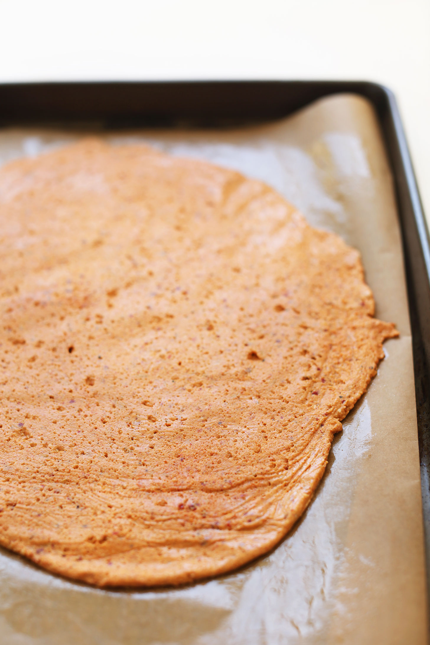 Spreading out vegan pepperoni dough on a parchment-lined baking sheet