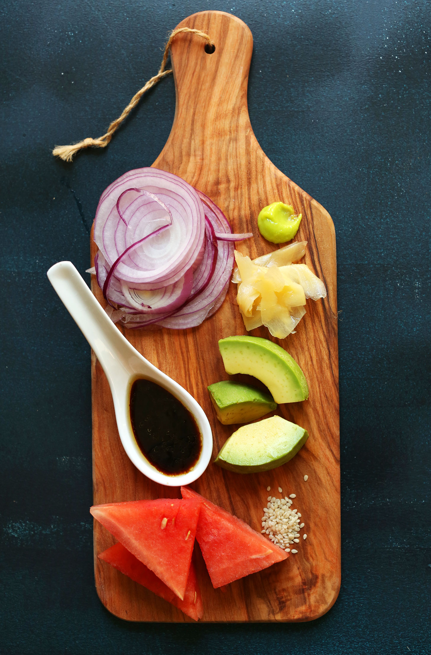 Wood cutting board with watermelon, avocado, onion, sesame seeds, pickled ginger, wasabi, and gluten-free tamari