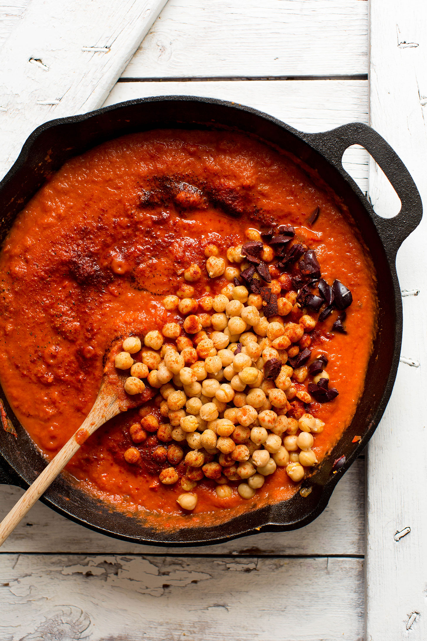 Stirring chickpeas into a cast-iron skillet filled with our gluten-free vegan Shakshuka recipe