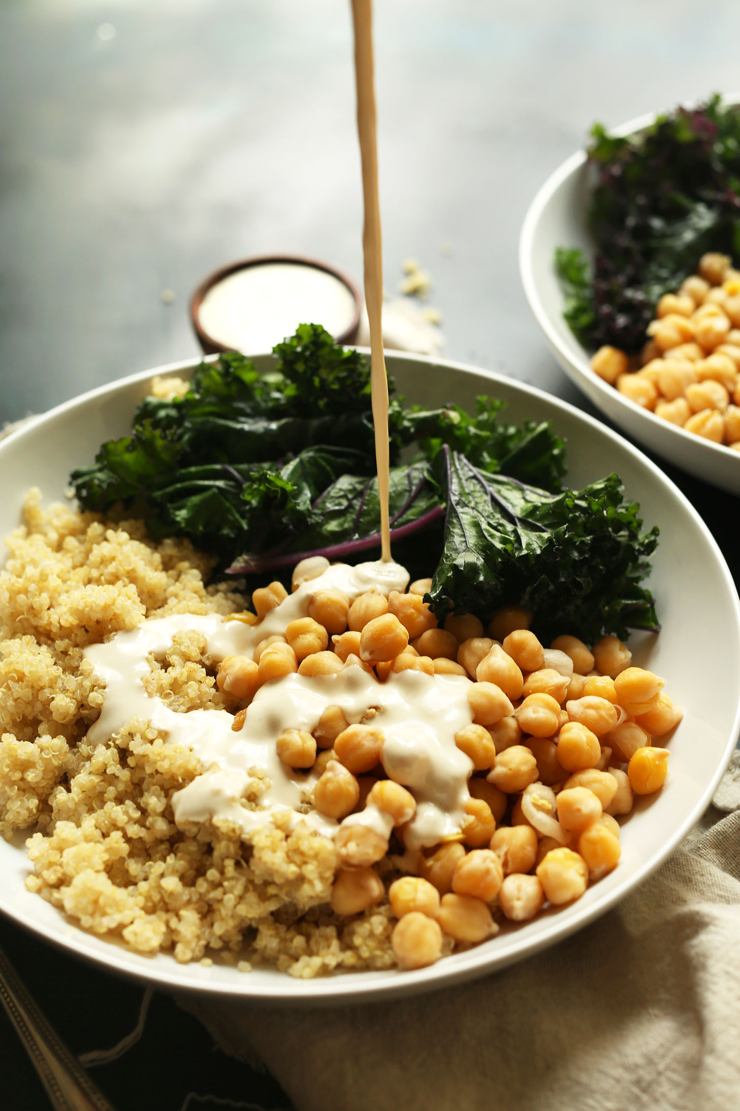 Pouring Tahini Sauce onto our Quinoa Chickpea Buddha Bowls for a simple gluten-free vegan meal