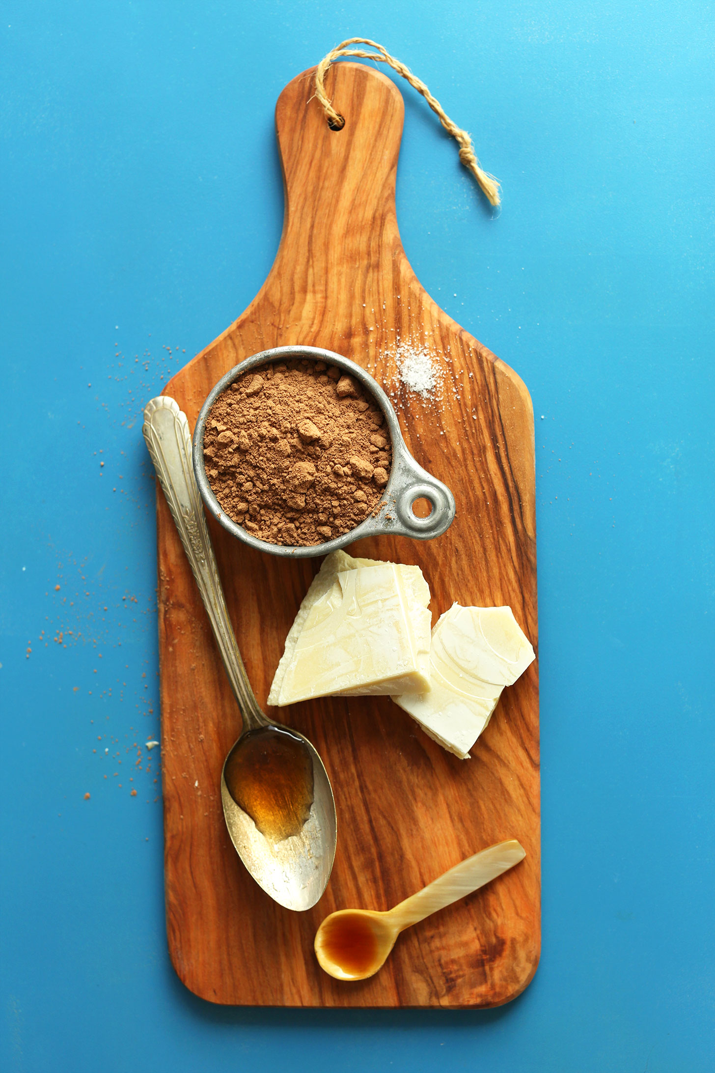 Cutting board showcasing cocoa powder, cacao butter, maple syrup, and vanilla for making homemade chocolate syrup