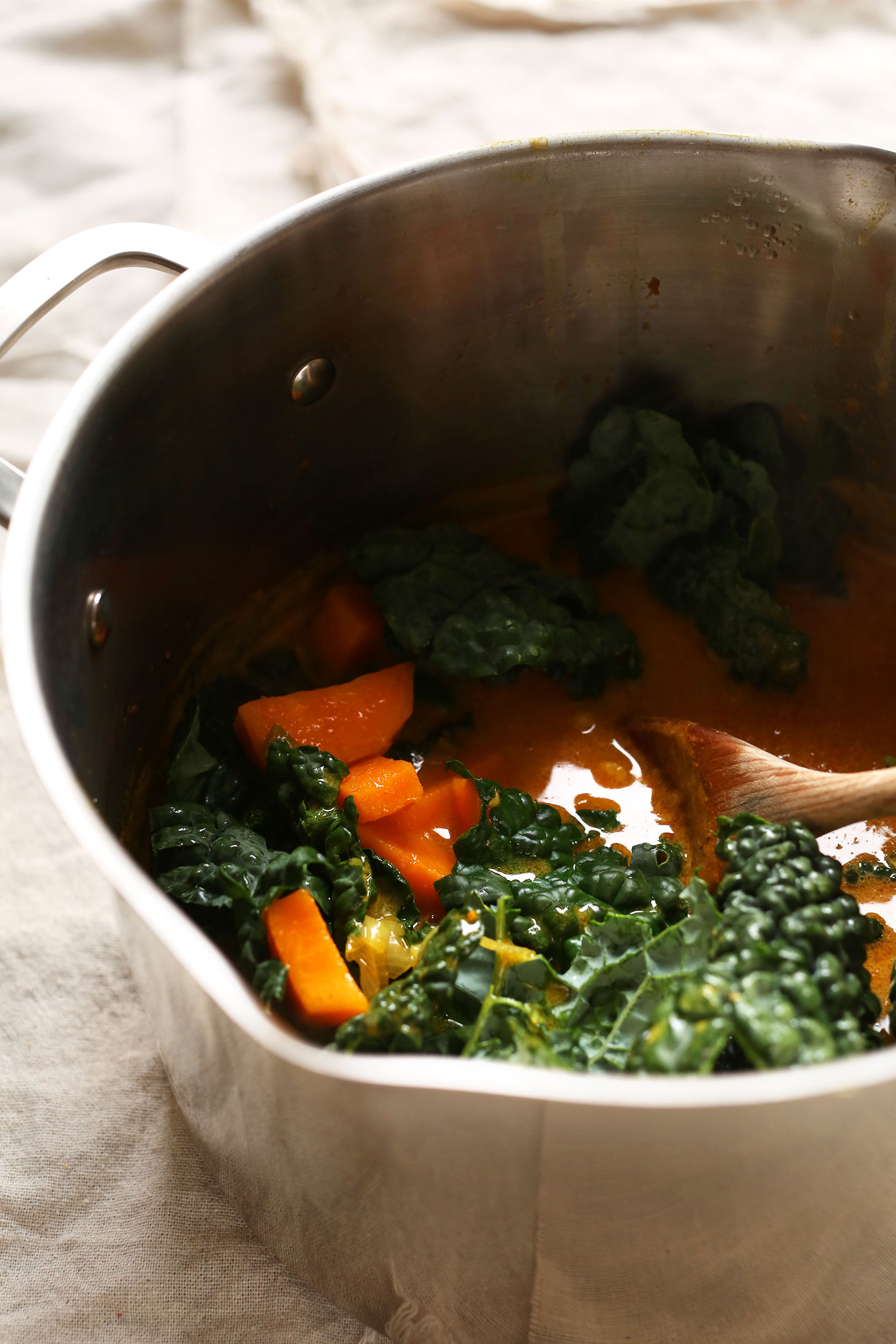 Using a wooden spoon to stir Sweet Potato Kale Curry for a protein-rich vegan dinner