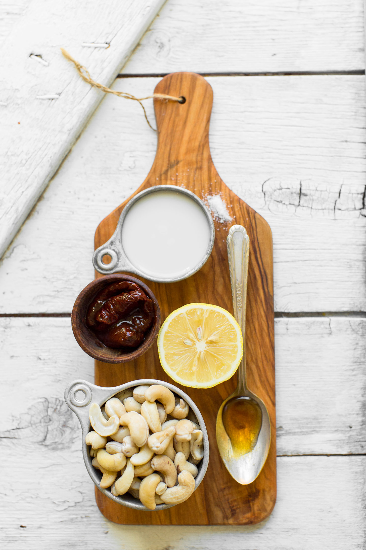 Wood cutting board with cashews, maple syrup, lemon, chipotle peppers, almond milk, and salt for making vegan chipotle aioli